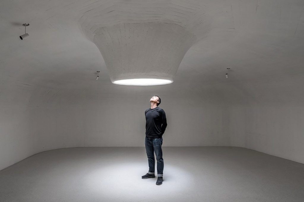 Man in darkened room looking through light portal in ceiling
